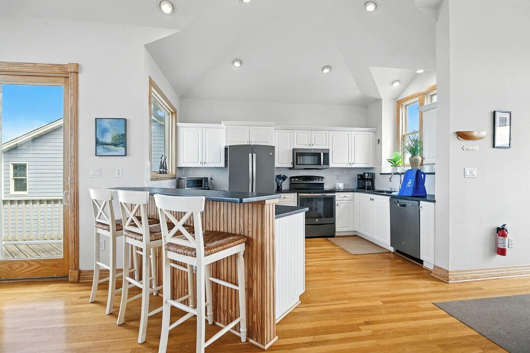 A modern kitchen with white cabinets, a central island with bar stools, a microwave, and a refrigerator.