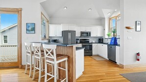 Una cocina moderna con armarios blancos, una isla central con taburetes y electrodomésticos como microondas y refrigerador.