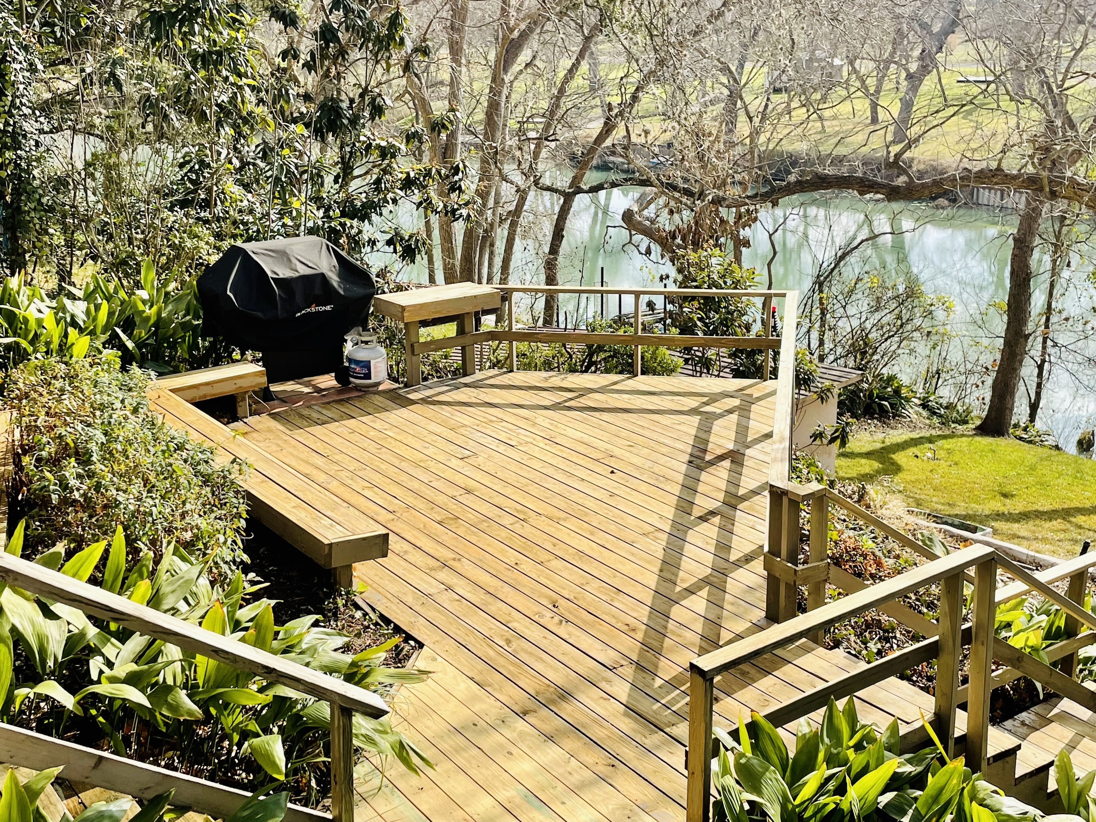 Una terraza de madera con una parrilla y zona de estar con vistas a un lago.
