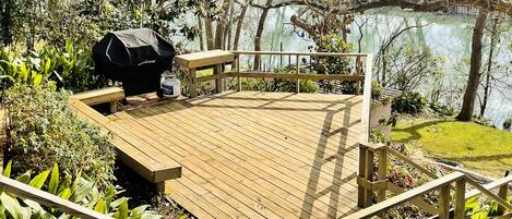 Una terraza de madera con una parrilla y zona de estar con vistas a un lago.
