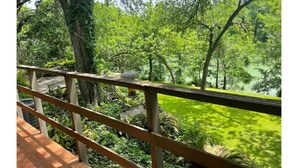 Eine Holzterrasse mit Geländer, die auf einen üppigen Garten mit Bäumen und einem Teich blickt.