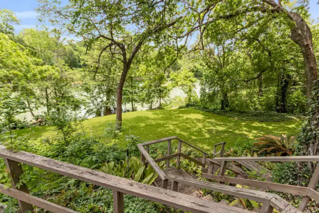 Un jardin luxuriant avec une terrasse en bois et des escaliers menant à une zone herbeuse.