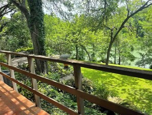 Una terraza de madera con barandilla que da a un jardín exuberante con árboles y un estanque.
