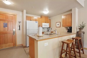 Compact kitchen area with a central island, refrigerator, microwave, sink, and bar stool.