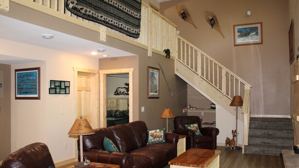 Un salón espacioso con un sofá de cuero marrón, una mesa de centro de madera y una escalera que conduce a un nivel superior.