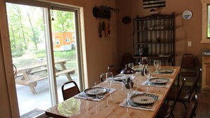 Un comedor con una mesa larga lista para una comida, un banco de madera afuera y una vista de una casa a través de una puerta de vidrio.