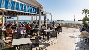 Un caffè all'aperto con tavoli e sedie, con vista sulla spiaggia.
