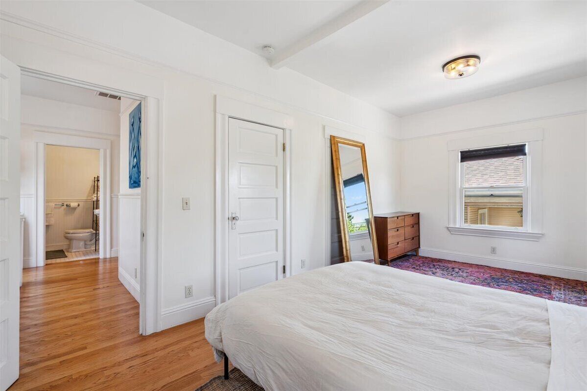 Un dormitorio con una cama grande, un aparador, un espejo y una ventana con persianas.