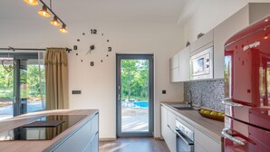 Uma cozinha moderna com micro-ondas embutido, geladeira vermelha e uma grande janela com vista para um jardim.