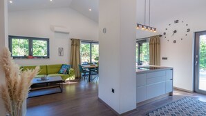 Cozinha moderna com ilha integrada, área de jantar com sofá verde e grandes janelas com vista para o verde.
