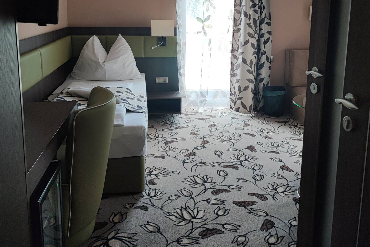 Hotellihuone, jossa on sänky, työpöytä, tuoli, televisio ja ikkuna, jossa on verhot.