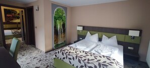 Habitación de hotel con cama, escritorio y ventana grande con vista a una cascada.