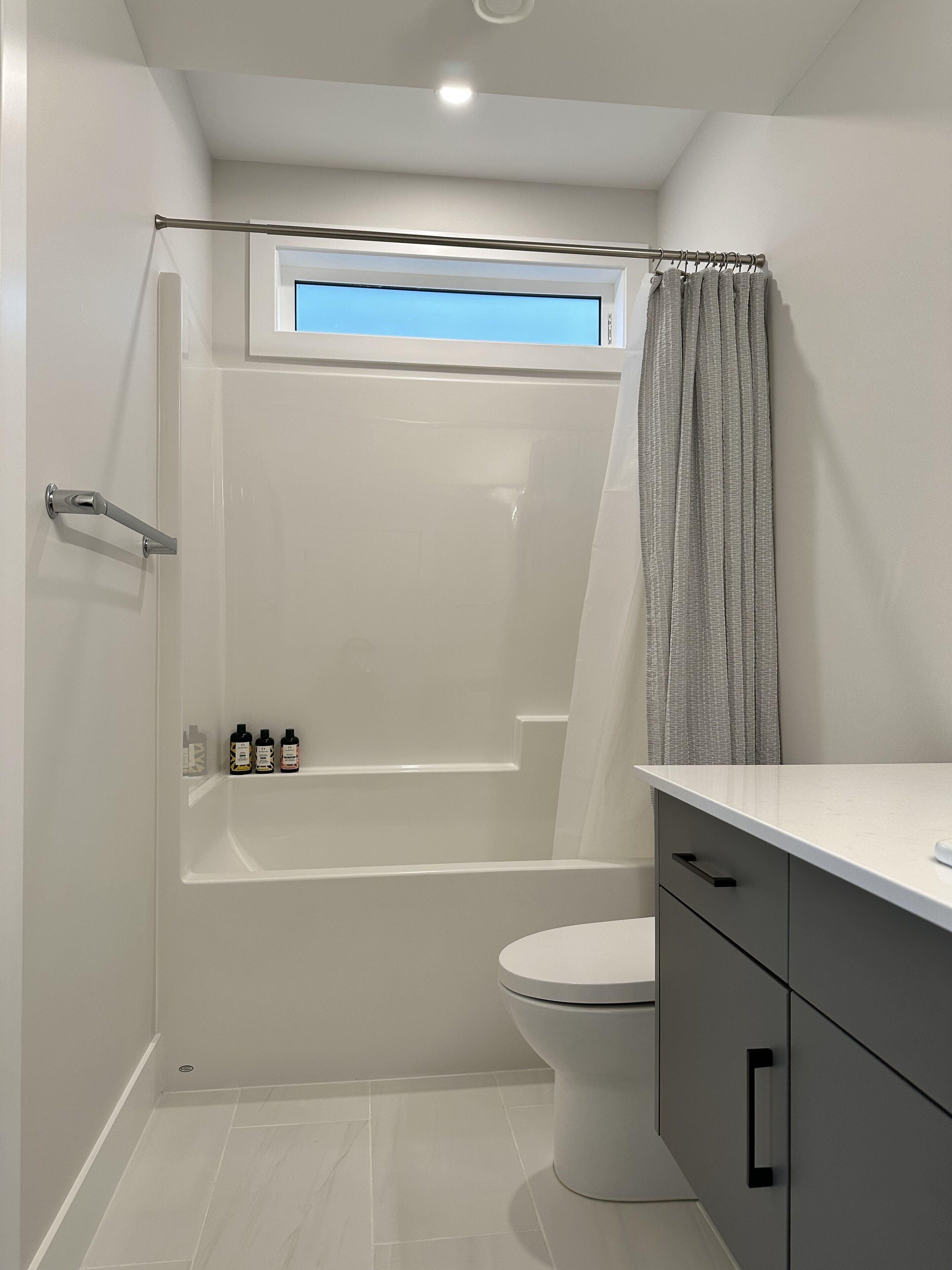 Un baño moderno con bañera, inodoro y ventana sobre la ducha.