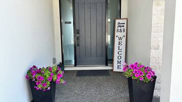 A modern entrance with a glass door, two black planters with pink flowers, and a sign with the text "Welcome Home."