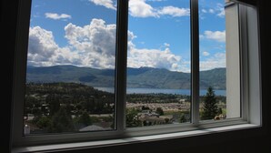 Uitzicht door een raam op een heldere lucht, bergen en een meer.