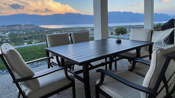 Een overdekt terras met een tafel en stoelen, met uitzicht op een schilderachtige berg- en merenlandschap.