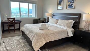 A bedroom with a large bed, a desk, a chair, two bedside lamps, and a view of the outdoors.