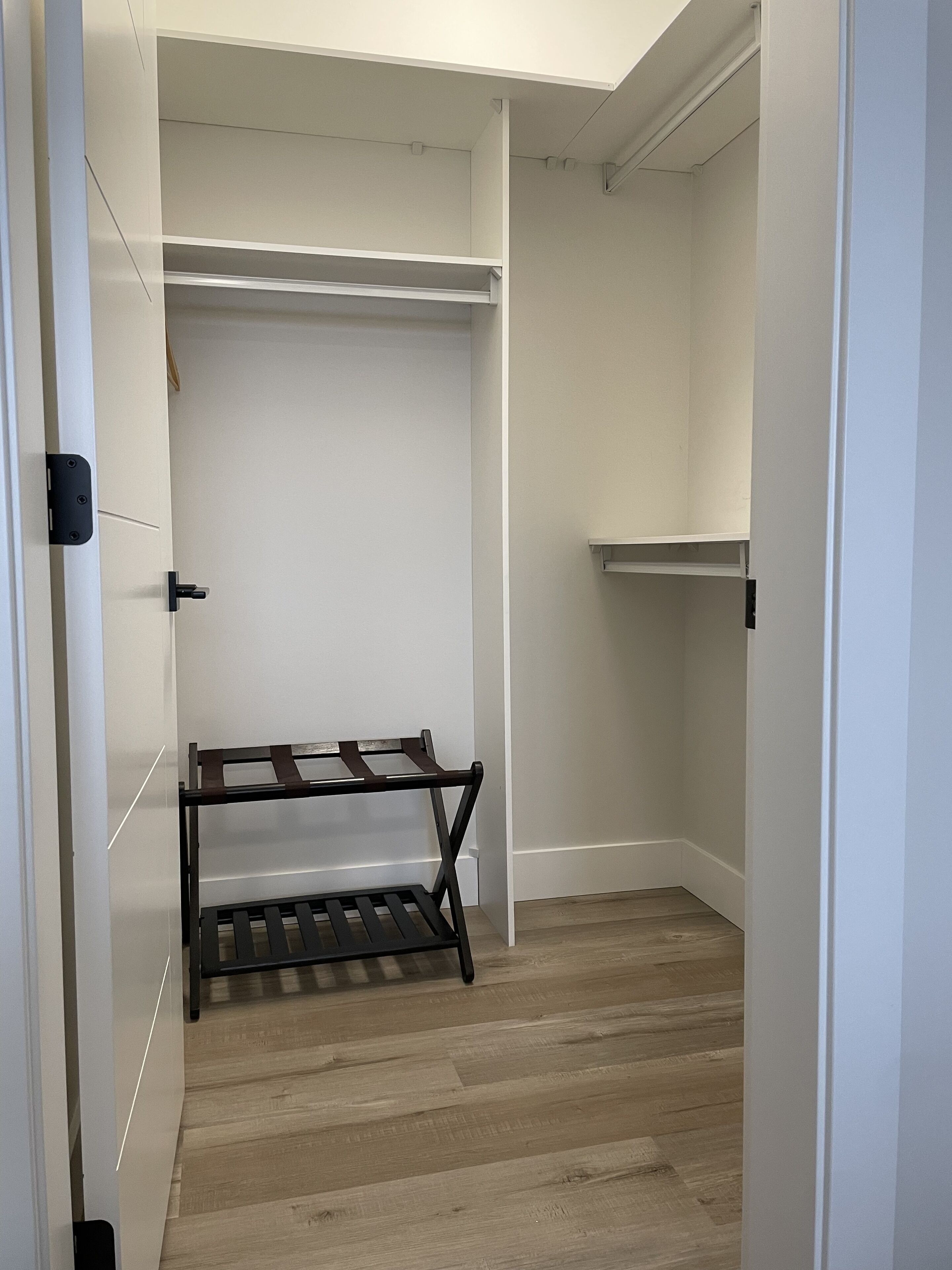A walk-in closet with wooden flooring, white walls, and a black metal rack.