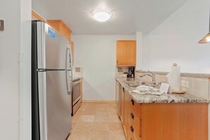 Kitchen area features a refrigerator, oven, and coffee maker.