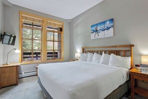 Relax in a spacious room with a large bed, a window offering a view of lush greenery, and a painting above the bed.