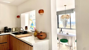 Eine moderne Küche mit einer großen Kochinsel, Blick auf den Strand und einem Essbereich mit Tisch und Stühlen.