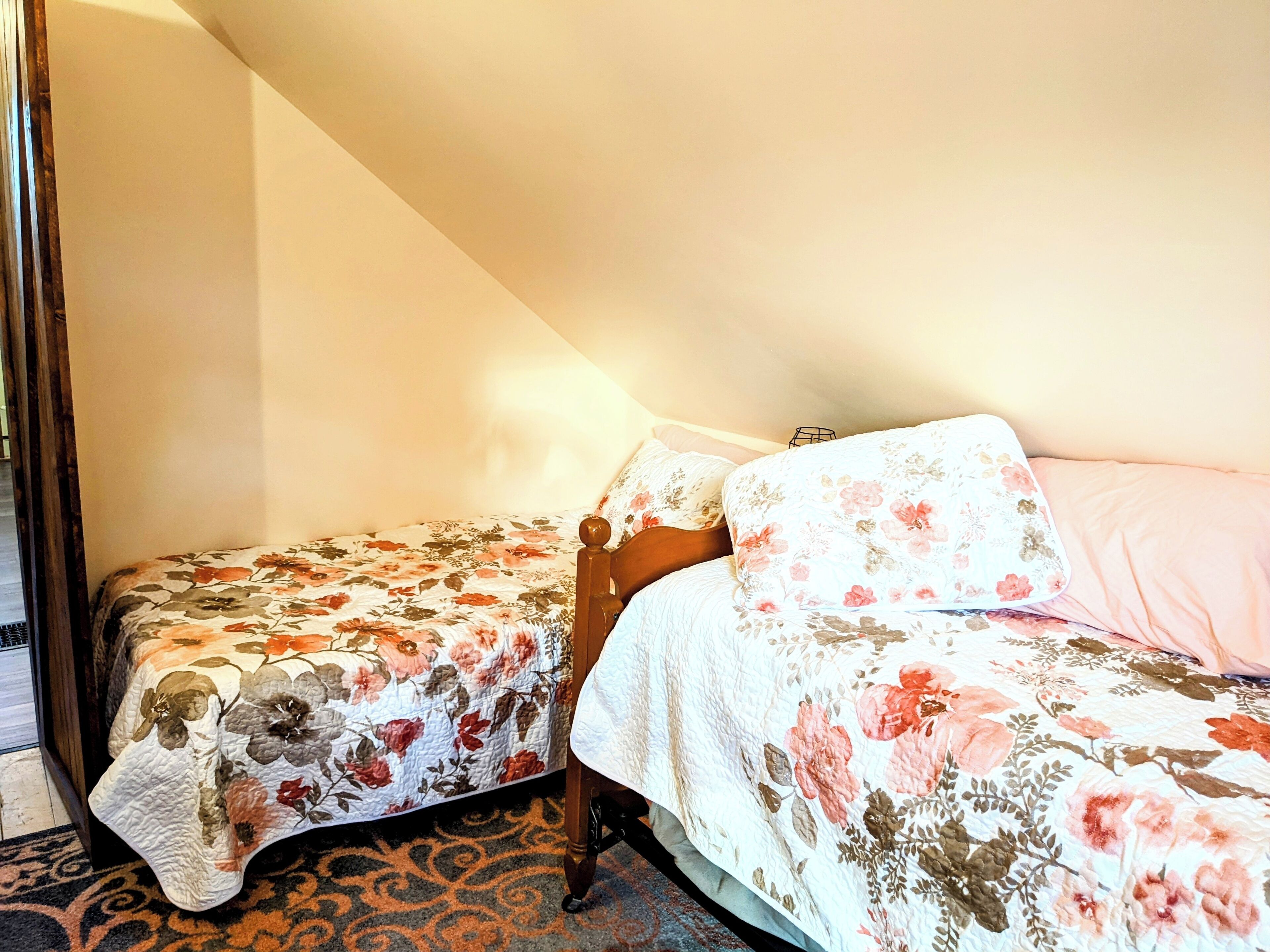Two beds with floral bedding in a room with a sloped ceiling and a patterned carpet.