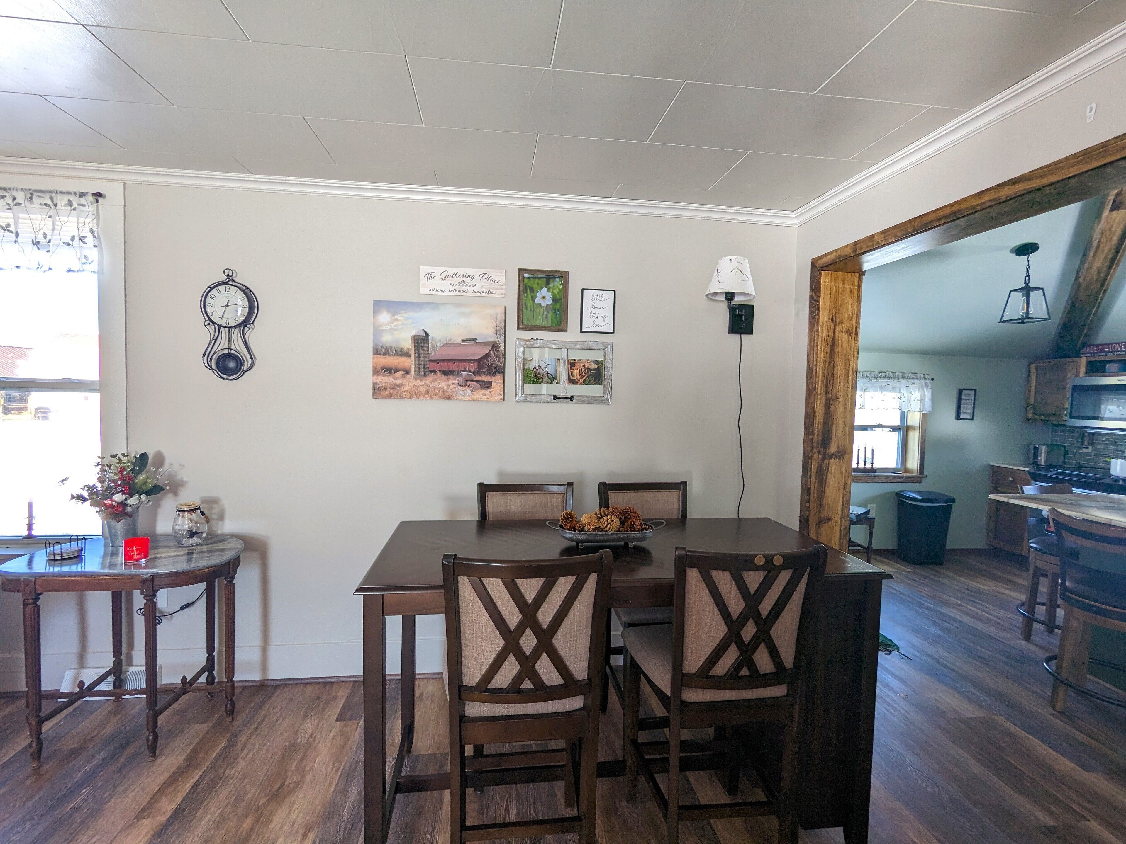 Un coin repas avec une table et des chaises en bois, une horloge et des tableaux encadrés accrochés au mur.