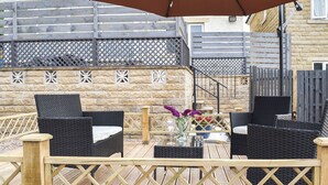 An outdoor patio area with wicker furniture, a wooden deck, and a stone wall. - Huddersfield House, Wood View (Huddersfield)