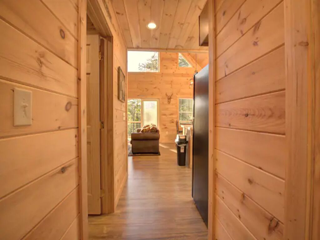 Un couloir intérieur en bois mène à un espace de vie comprenant un canapé et un réfrigérateur.