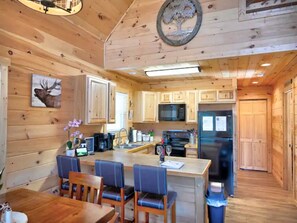A wooden cabin interior with a kitchen, dining area, and a large wooden door.