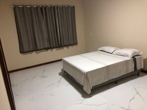 Un dormitorio con cama, ropa de cama blanca, suelo de mármol y cortina gris.