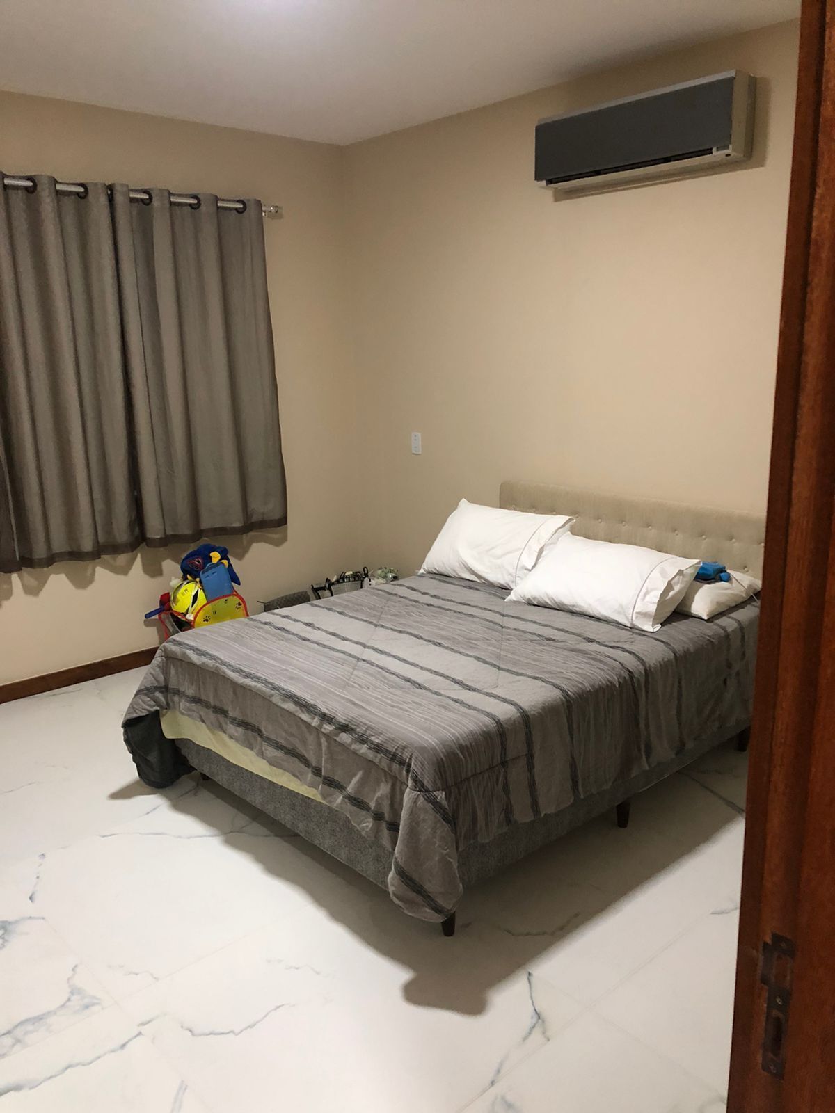 A bedroom with a bed, curtains, an air conditioning unit, and a toy on the floor.