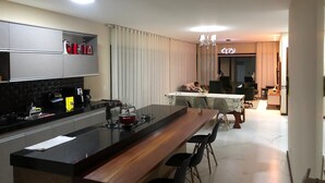 Ett modernt kök med en köksö i mitten, en matplats med bord och stolar samt ett vardagsrum med soffa och TV.