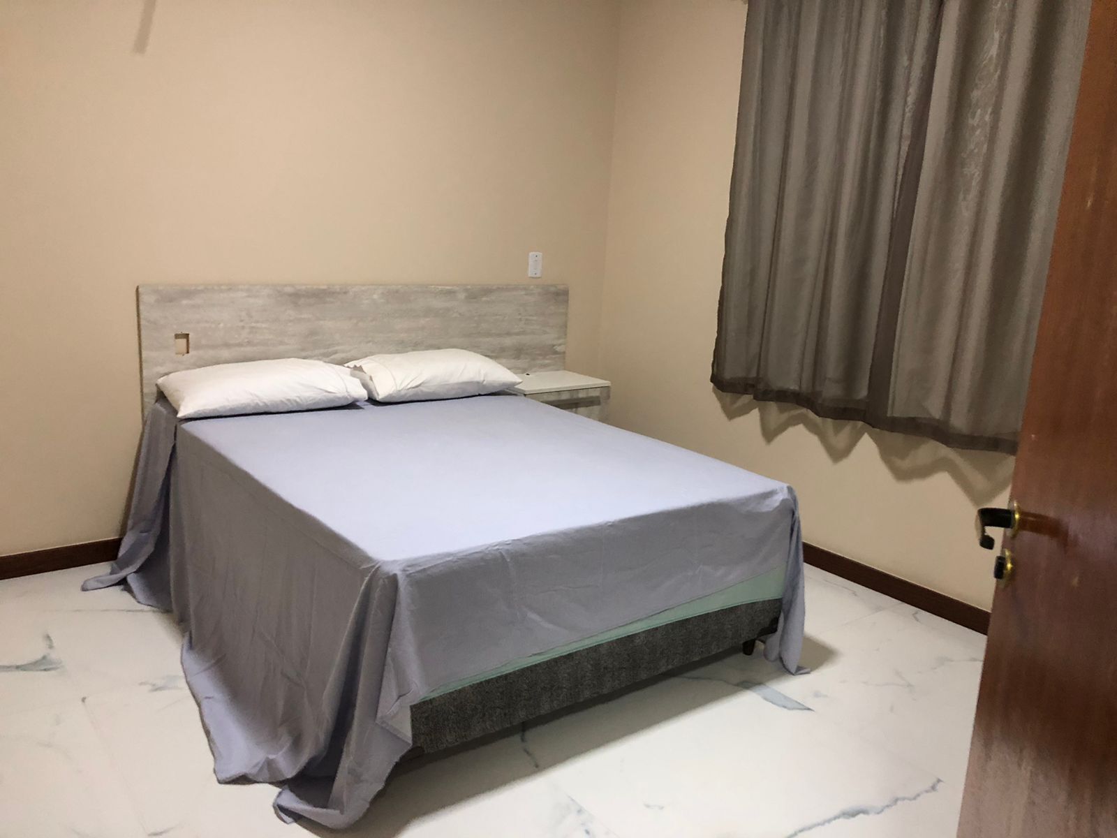 Une chambre à coucher avec un lit, des oreillers, une table de chevet et une fenêtre avec des rideaux.