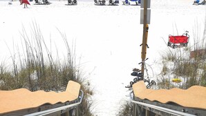 A beach with a wooden walkway leading to the sand, beach chairs, umbrellas, and a red wagon. - Sunsets on Water - private beach, pier, boat dock, fishing -12m to Navarre Beach (Navarre)