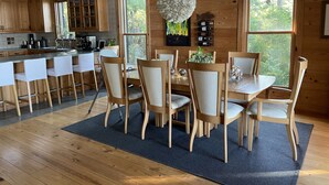 A modern kitchen with wooden cabinets, a dining area with a round table and chairs, and large windows offering a view of the outdoors. - Sunsets on Water - private beach, pier, boat dock, fishing -12m to Navarre Beach (Navarre)