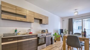 A modern kitchen with wooden cabinets, a built-in oven, and a dining area with a table and chairs. - Central and cosy one bedroom apartment KBON1-1 (Pieta)