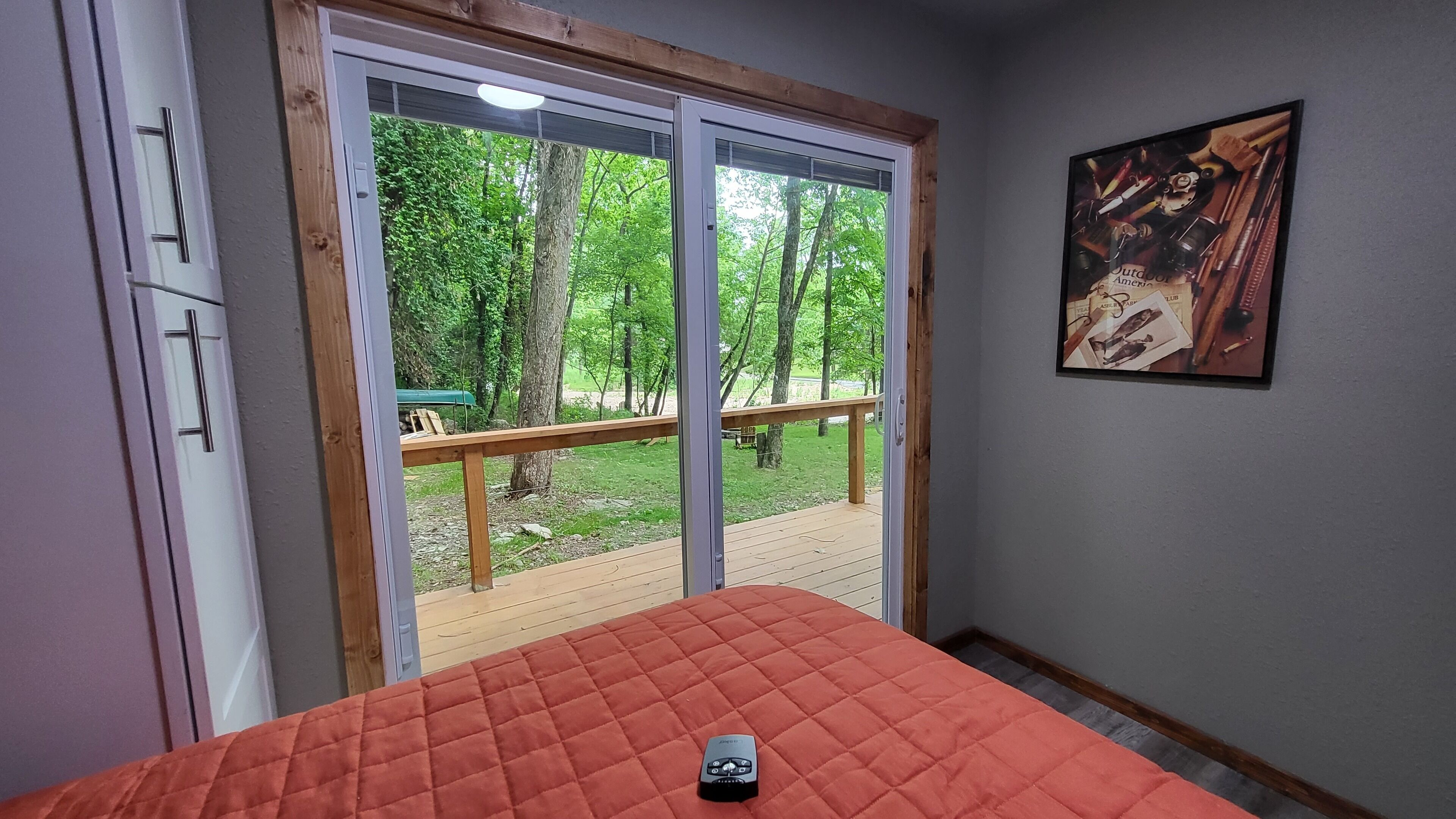 Ein Schlafzimmer mit einer großen Schiebeglasdoor, einem Bett mit roter Steppdecke und einem gerahmten Bild an der Wand.