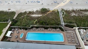 Vista aérea de un complejo turístico frente a la playa, con piscina, sillas de playa y sombrillas.