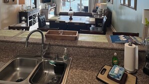 Una cocina con encimeras de granito, un lavamanos de acero inoxidable y un comedor con candelabro.