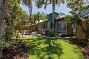 Una casa con jardín trasero que incluye un putting green, muebles de exterior y una cerca de madera.