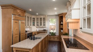 A kitchen with wooden cabinets, a granite countertop, a built-in oven, and a window with a view of greenery. - “Steeped in History” Exquisite 1919 Craftsman (Saint Augustine)