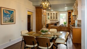 A modern kitchen with wooden cabinets, a glass dining table, and a chandelier. - “Steeped in History” Exquisite 1919 Craftsman (Saint Augustine)