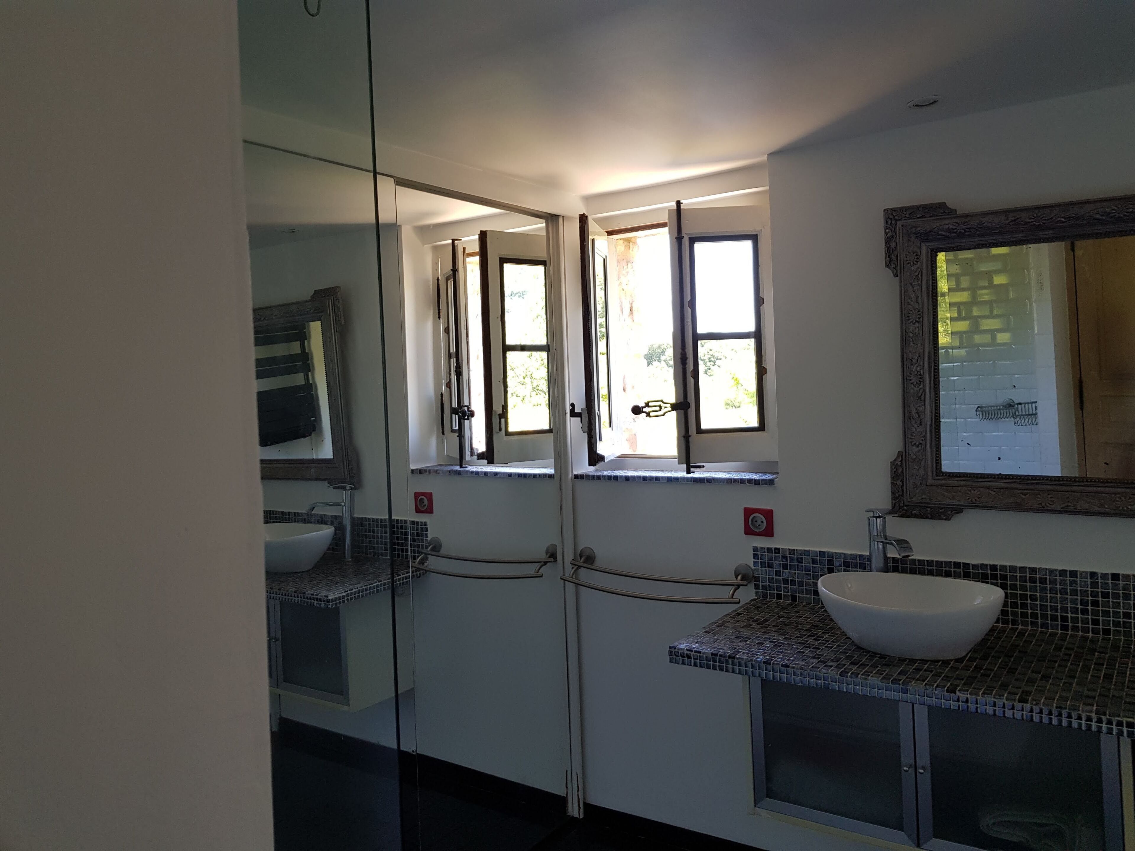 A bathroom with a large mirror, a sink, and a window with a view of greenery outside.