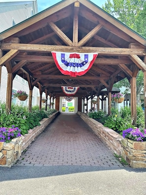 A covered walkway with a brick pathway, wooden beams, and hanging flower baskets.