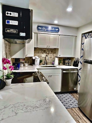 A modern kitchen with white cabinets, a marble countertop, and a stainless steel dishwasher.