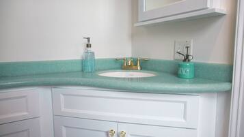 Een badkamer met een wit wastafelmeubel, een turquoise aanrechtblad, een gouden kraan en een zeegroene zeepdispenser.