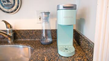 A kitchen counter with a sink, a glass carafe, and a teal-colored electric kettle.