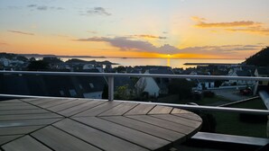 Ein Holztisch mit Stühlen auf einem Balkon mit Blick auf eine Wohngegend bei Sonnenuntergang.