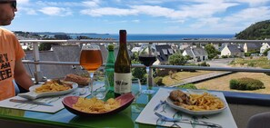 A dining table with food and drinks, overlooking a coastal view. - Quiet vacation rental with an exceptional ocean view in the hills above Erquy, Tu Est Roc + Park (Erquy)